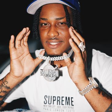 Man holding a diamond-encrusted chain pendant that says "DMAC".