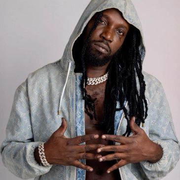 Man with dreadlocks wearing a hooded jacket and jewelry.