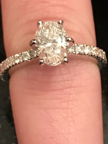 Elegant oval diamond ring with side stones on a finger.