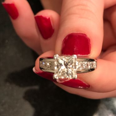 Close-up of a hand with red nail polish holding a diamond ring.