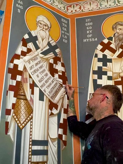 Artist painting a religious mural of Saint Gregory on a wall.