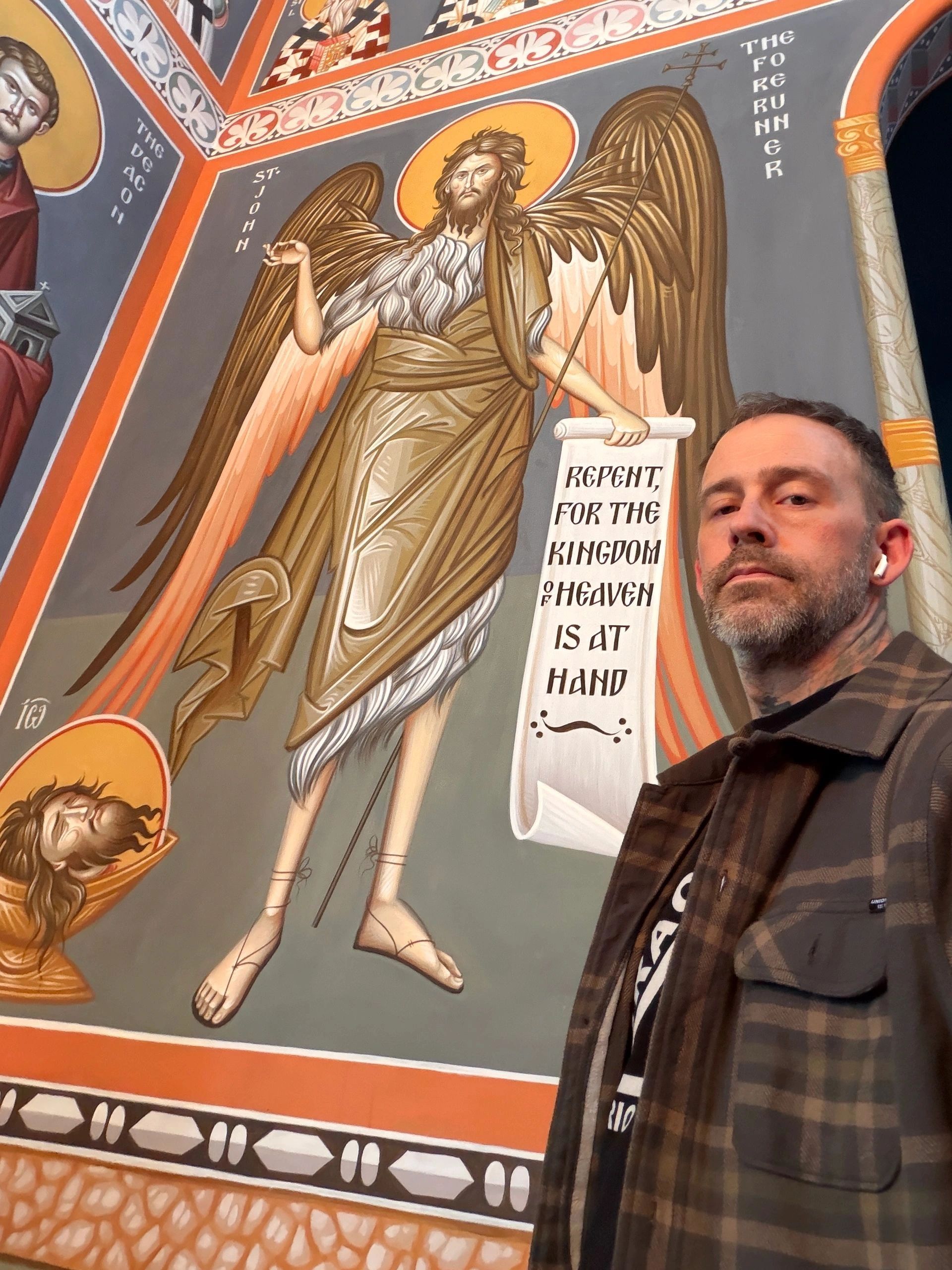 Man taking selfie in front of detailed religious mural featuring St. John the Forerunner.
