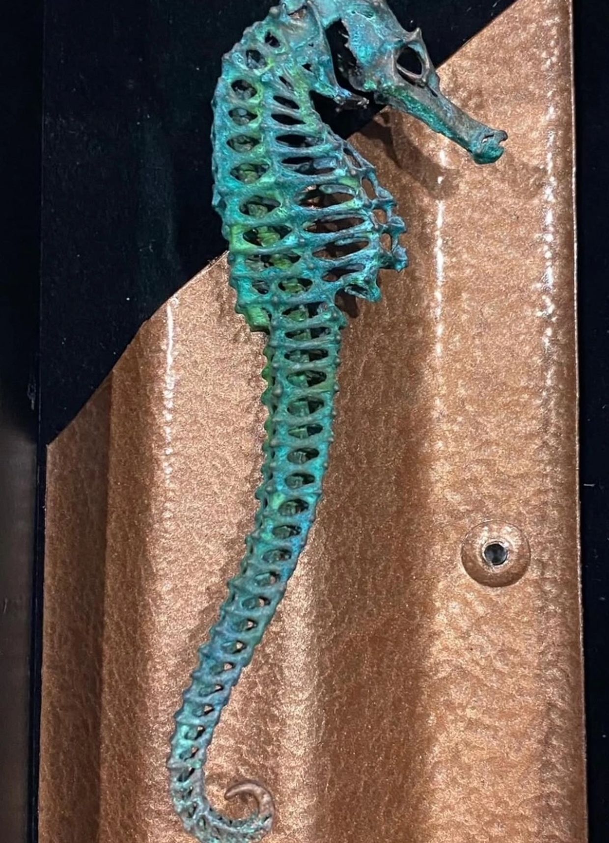 Intricately designed metal seahorse sculpture with a turquoise patina on a bronze background.