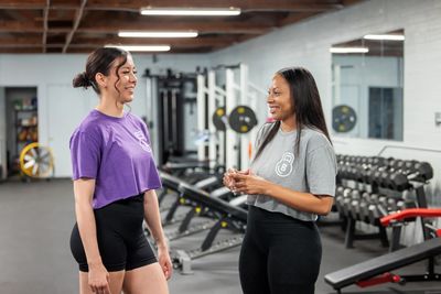 Two women chatting happily in a gym setting.
