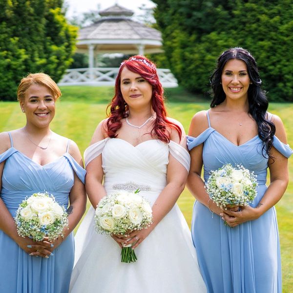 Bride with two bridesmaids in light blue dresses holding white bouquets outdoors.
