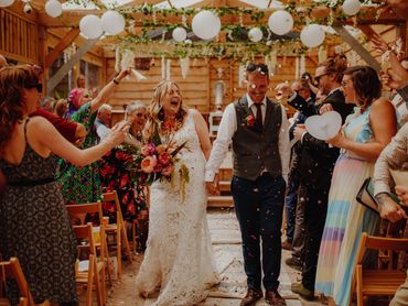 Joyful bride and groom walking down the aisle amid confetti and cheering guests.