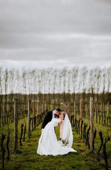 Bride and groom sharing a romantic kiss in a vineyard.