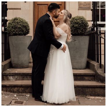 A newlywed couple sharing a kiss outside a hotel entrance.