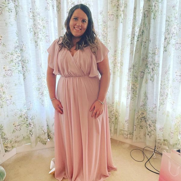 Woman in a flowing pink gown standing in front of floral curtains.