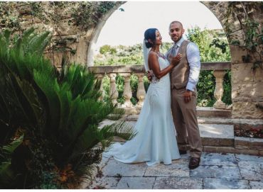 Newlywed couple posing happily under a stone arch with lush greenery.