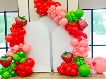 Strawberry-themed balloon arch with red, pink, and green balloons.