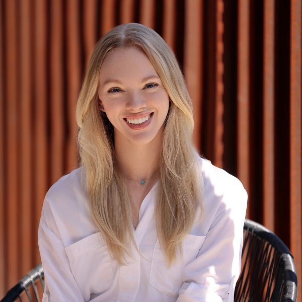 Smiling woman with long blonde hair against a striped wooden background.