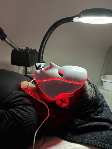 Person wearing a LED light therapy mask under a lamp.