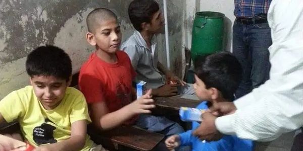 Children sitting indoors, receiving milk cartons from an adult.