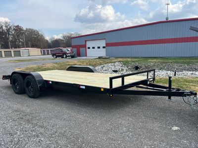 Black flatbed trailer with wooden deck parked outside near a building.