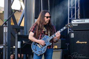 Long-haired man playing electric guitar on stage at a live concert.