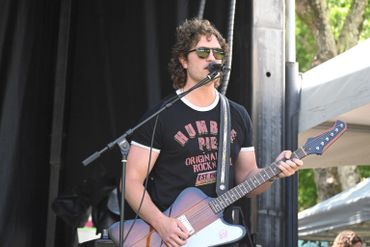 A male musician playing guitar and singing on stage.