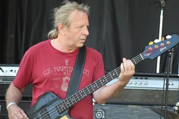 Man playing bass guitar on stage wearing a red shirt.