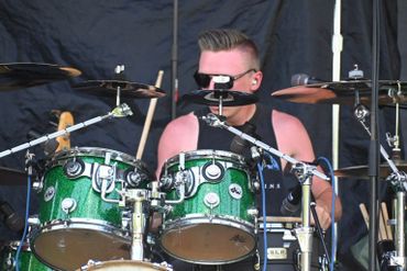 Drummer playing a green drum set on stage during a live performance.