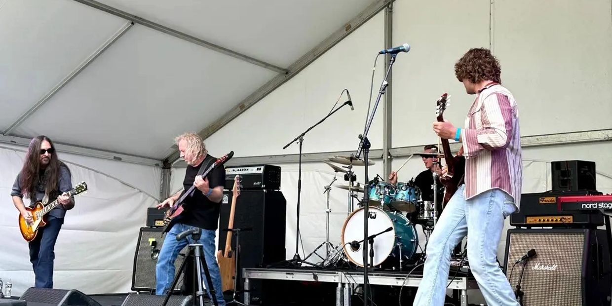 A four-member band performs live on an outdoor stage under a tent.