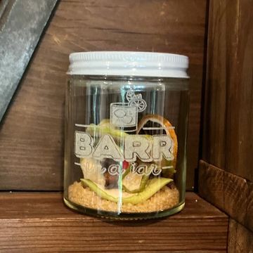 Glass jar with fruit and crumbs inside on wooden shelf.