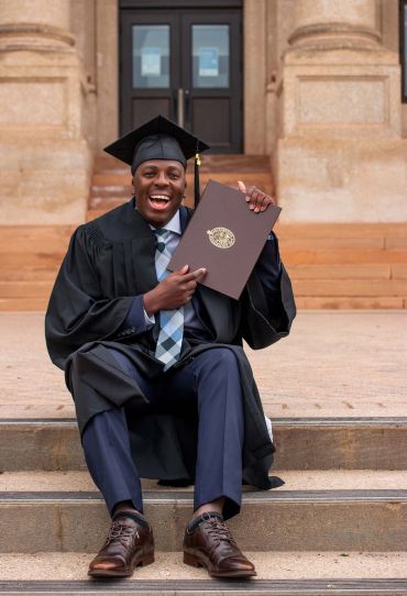 Excited graduate proudly holding diploma on steps.