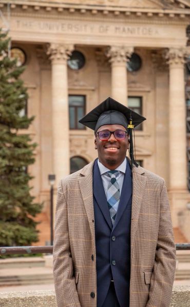 Graduate in cap and gown standing in front of a university building.