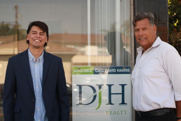 Two men standing beside a realty sign for David Harris Realty.