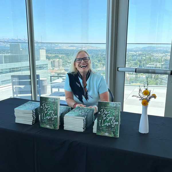 Author Kathryn Henry smiling behind a table with stacks of her book A Dime to Say I Love You