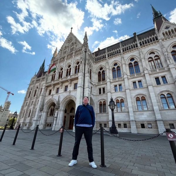 Person stands in front of a grand historic building with ornate architecture.
