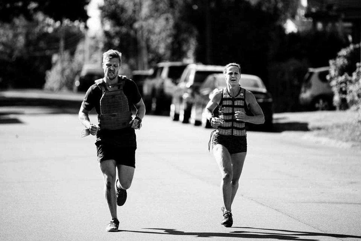Two athletes running wearing weighted vests for a CrossFit workout.
