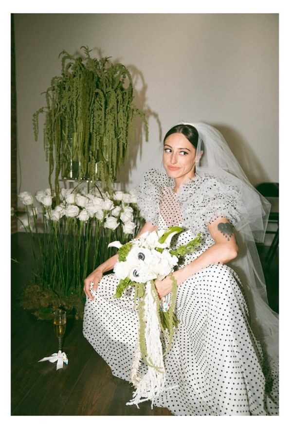 Bride posing with reception flower instillation with bouquet and polka dot dress