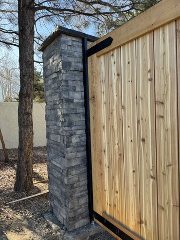 A wooden gate attached to a stone pillar in an outdoor setting.
