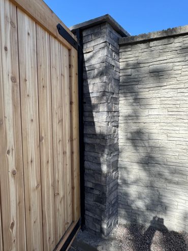 Wooden gate next to a stone pillar and wall under clear blue sky.