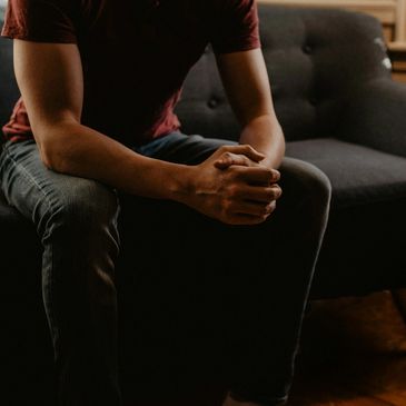 Person sitting on a couch with hands clasped, looking contemplative.