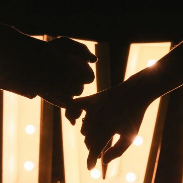 Two hands gently holding each other against a warm, glowing light.