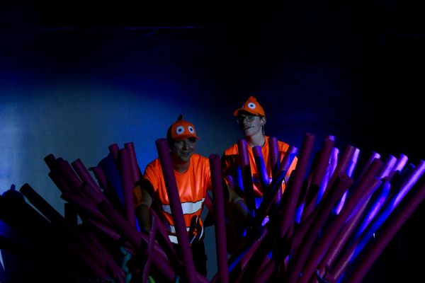 Two people dressed as clownfish with foam sticks in blue light.