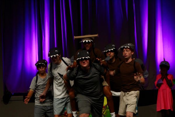 Group of people in dinosaur hats performing on stage.