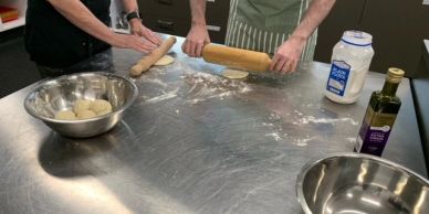 Two people rolling dough on a metal table.