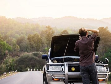 Man stands puzzled by his broken-down car on a rural road.