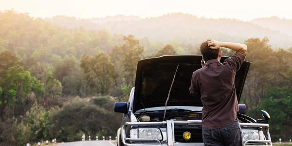 Man stands confused by his broken car on a rural road.