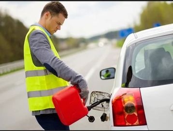Man in yellow vest refueling a white car with a red gas can on the roadside.