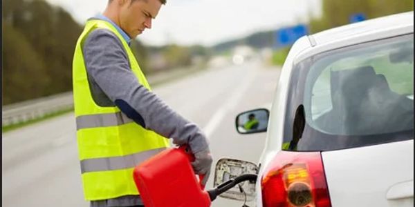 Man in a reflective vest refueling a car with a red gas can on the roadside.