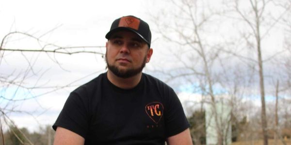 Man in black t-shirt and cap outdoors.