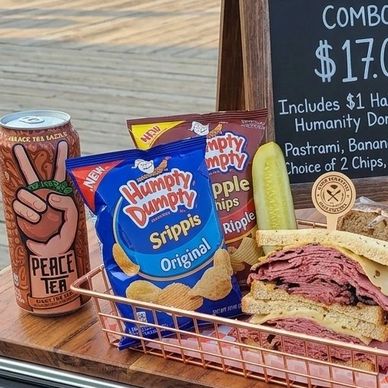 A sandwich combo with chips, a pickle, and a canned drink on a wooden table.