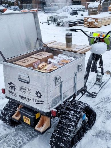 Tracked bike delivering food in snowy construction site.