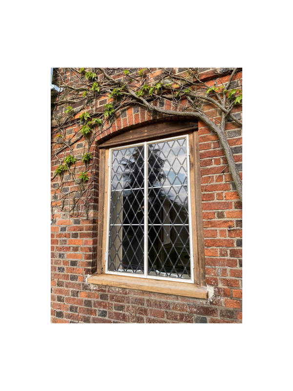 A diamond-pane window set in a red brick wall with ivy vines growing around it.