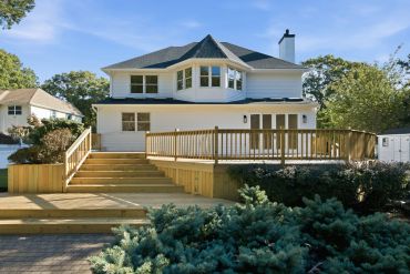 Large white two-story house with a wooden deck and stairs.