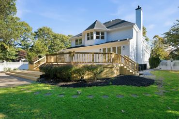 White two-story house with a wooden deck and green lawn.