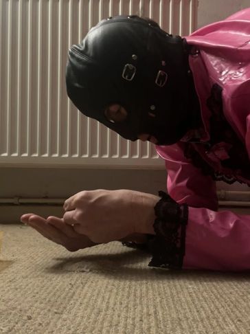 Person in a black leather mask and pink outfit lying on the floor.